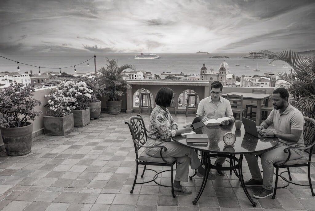 Tres estudiantes con Biblias y portátiles en una terraza con vista a la ciudad colonial y al mar Caribe